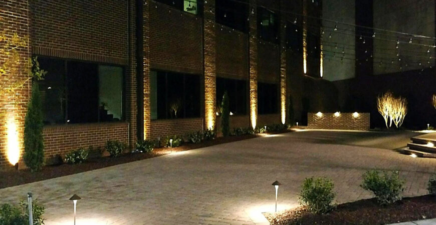 Commercial lighting installed within landscaping outside of a building lights the path to the front door